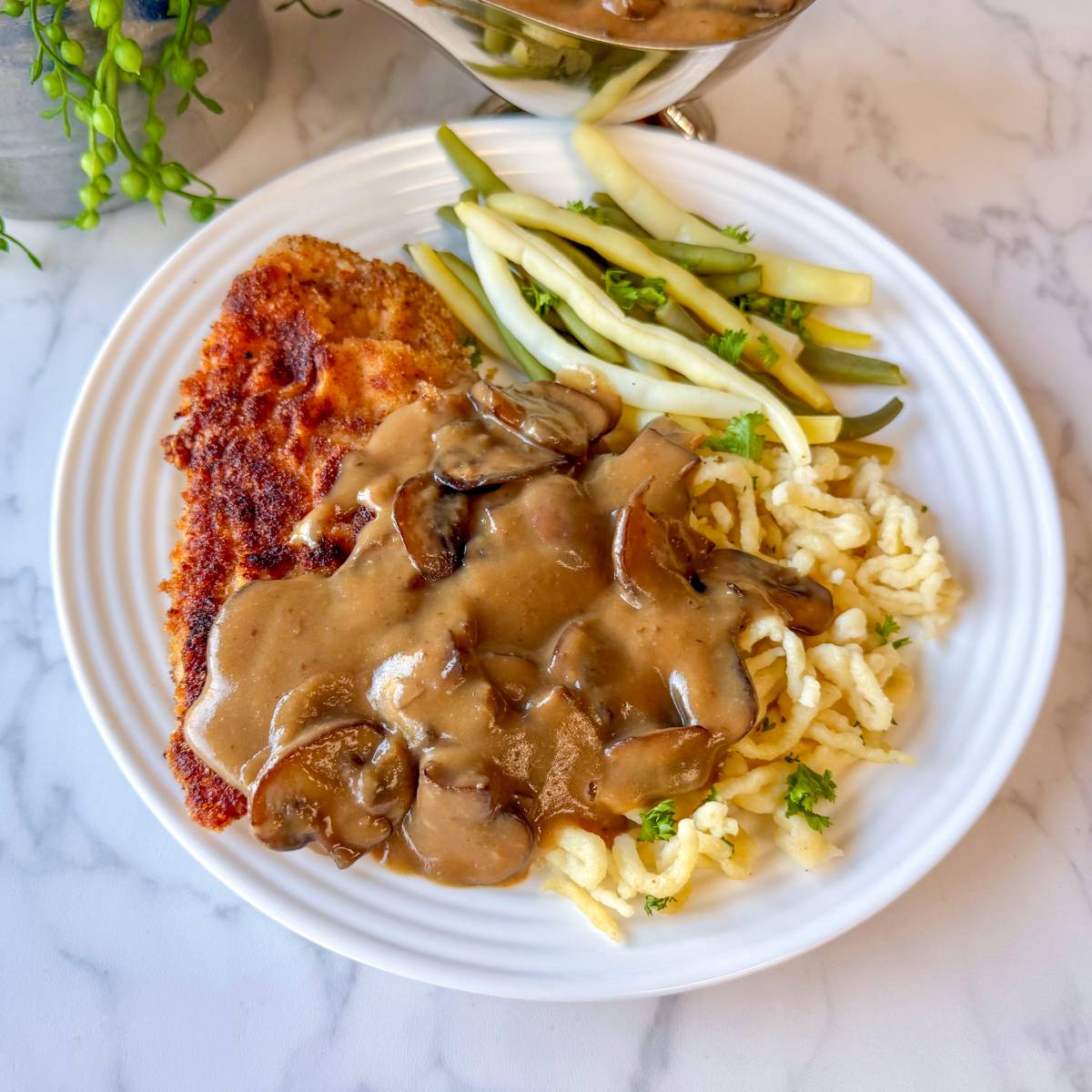 schnitzel with spaetzle covered with mushroom sauce next to beans on white plate