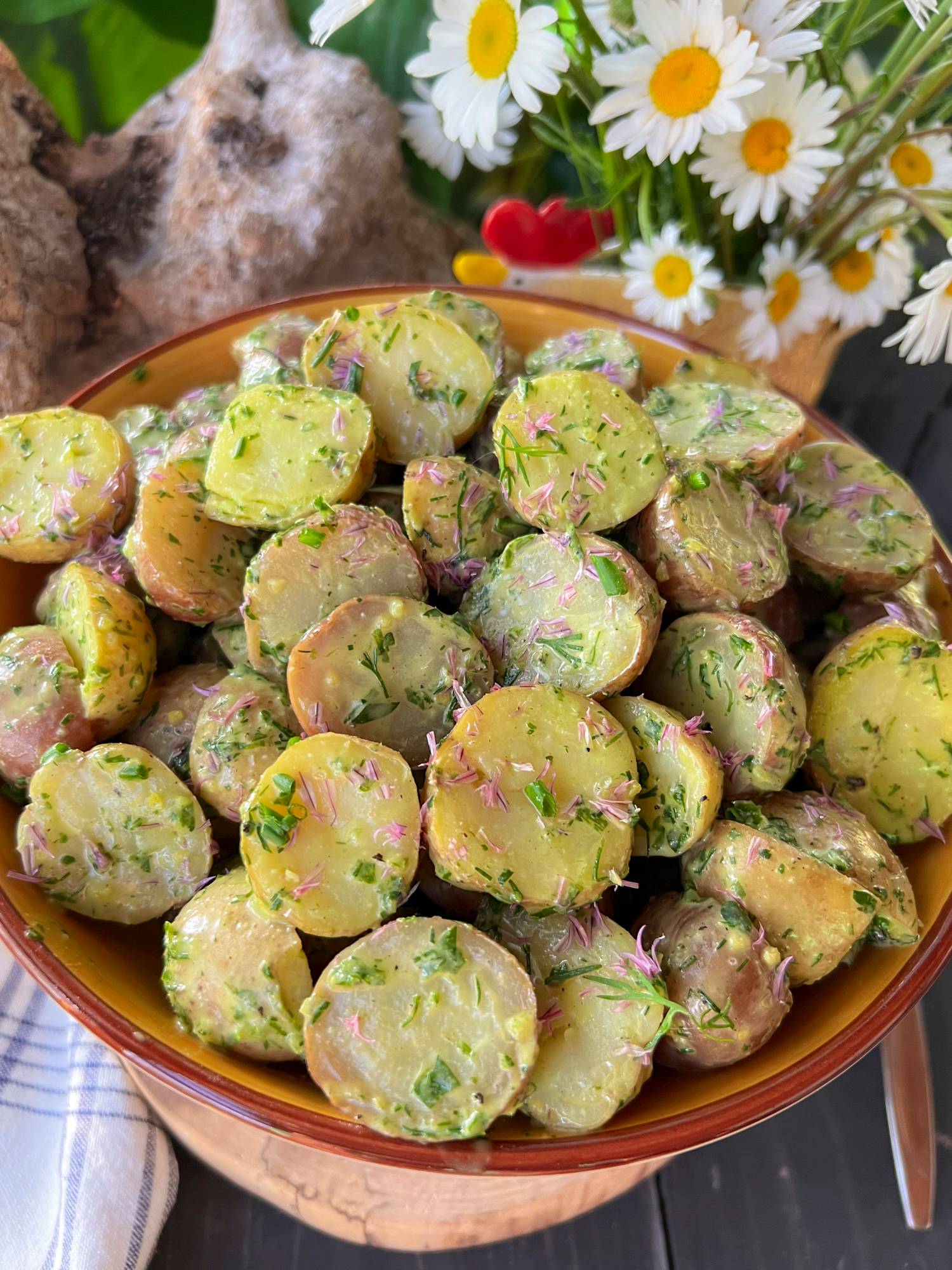 fresh baby potatoes in a creamy vinaigrette with plenty of fresh herbs in a bowl with daisies 