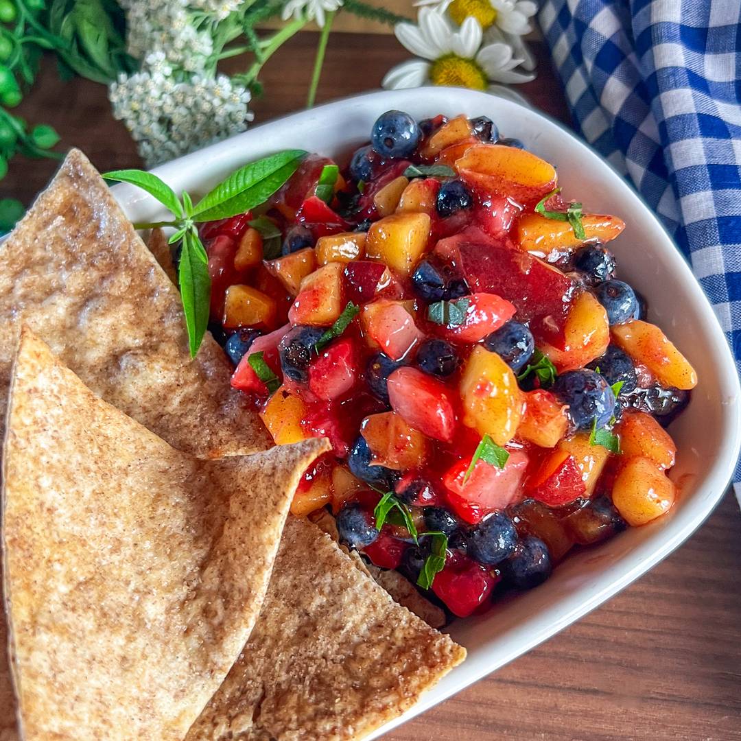 small diced peaches, strawberries and blueberries in white dish with crispy cinnamon chips