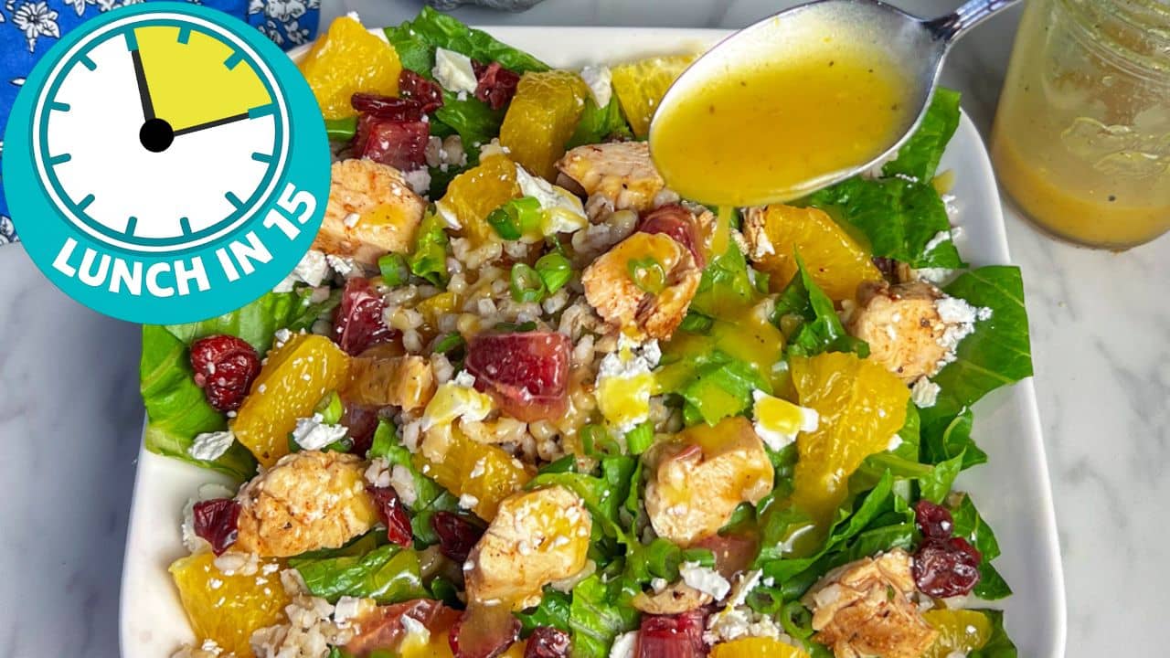green salad with pieces of chicken and oranges with spoon holding salad dressing