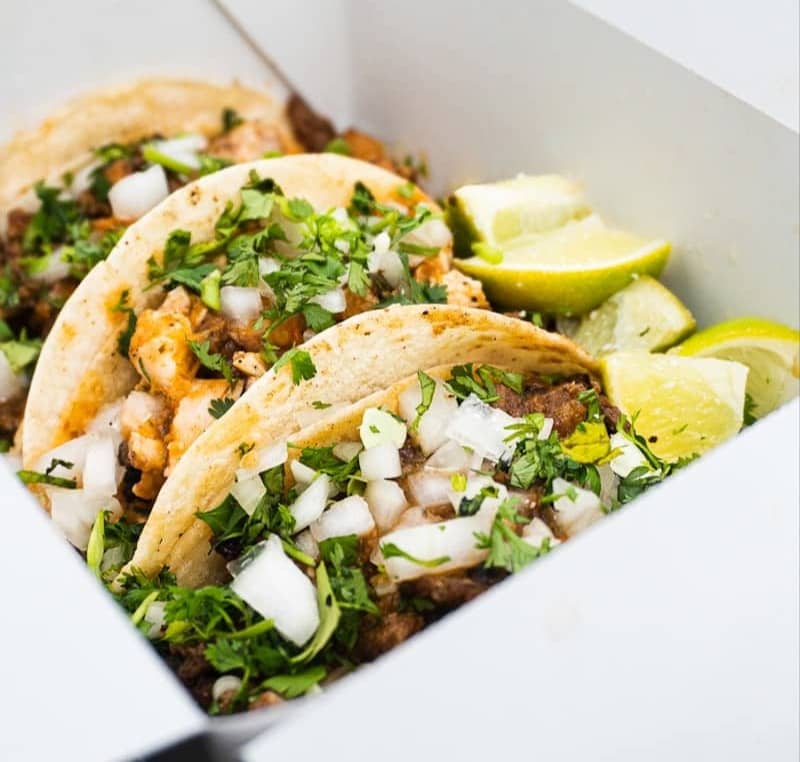Three tacos with lime wedges in a white box