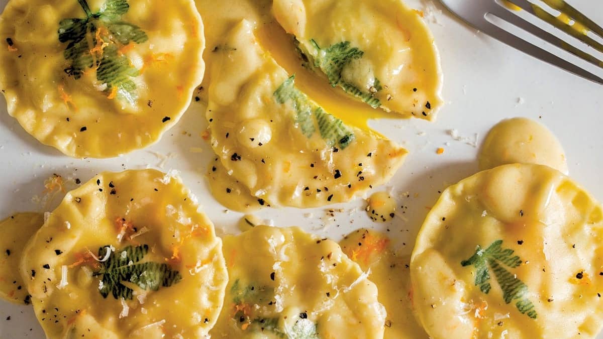 Close up of poached yolk stuffed ravioli with yolk running onto plate.