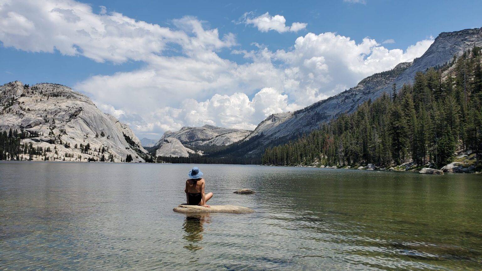 Women sitting on rock in a lake surrounded by granite cliffs and evergreen trees