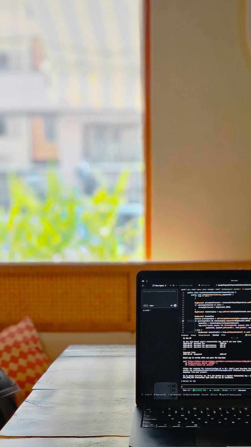 Laptop displaying code on a wooden table by window.