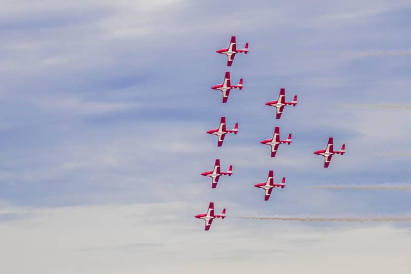 Nine jets climb in a perfect triangle, crisp smoke trails against a soft blue sky, a clean aviation scene symbolizing leadership, direction, momentum and collective excellence.