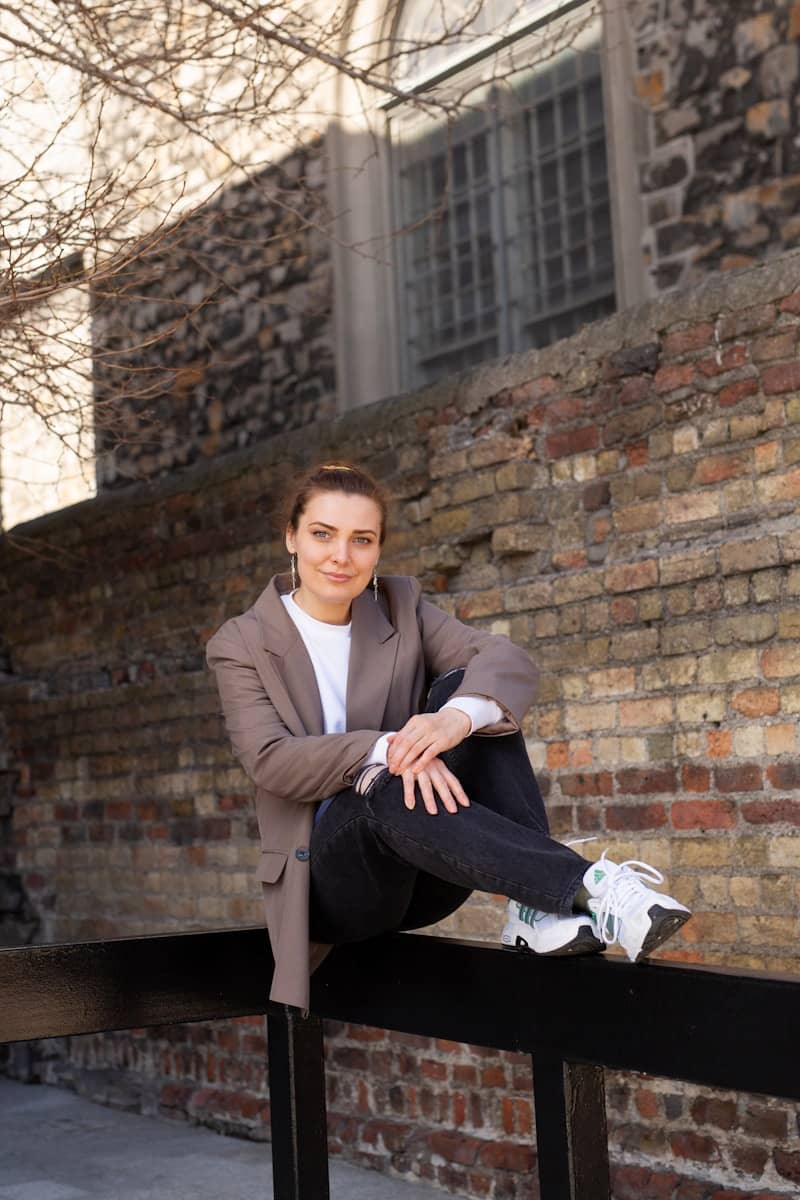 Woman in blazer sitting on railing near brick wall