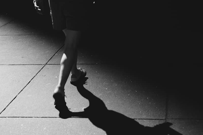 Person's legs and shadow on pavement in strong light.