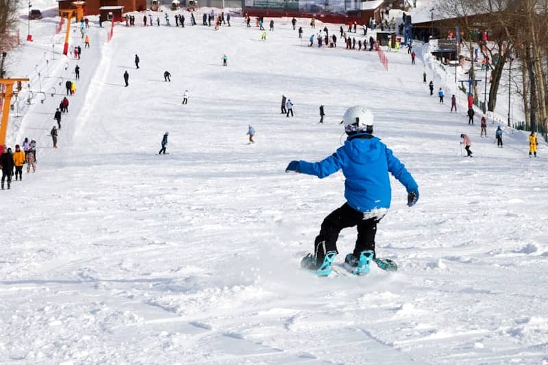 A snowboarder riding down a snowy slope with others.