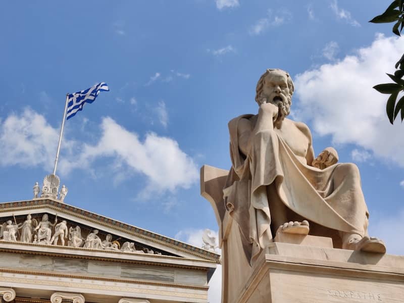 Statue of socrates in front of a greek flag.