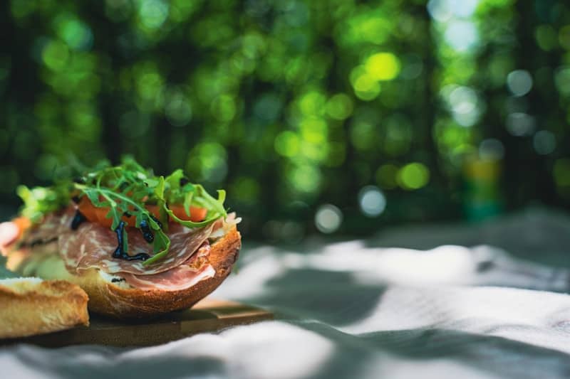 Gourmet sandwich with prosciutto and arugula on a picnic blanket.