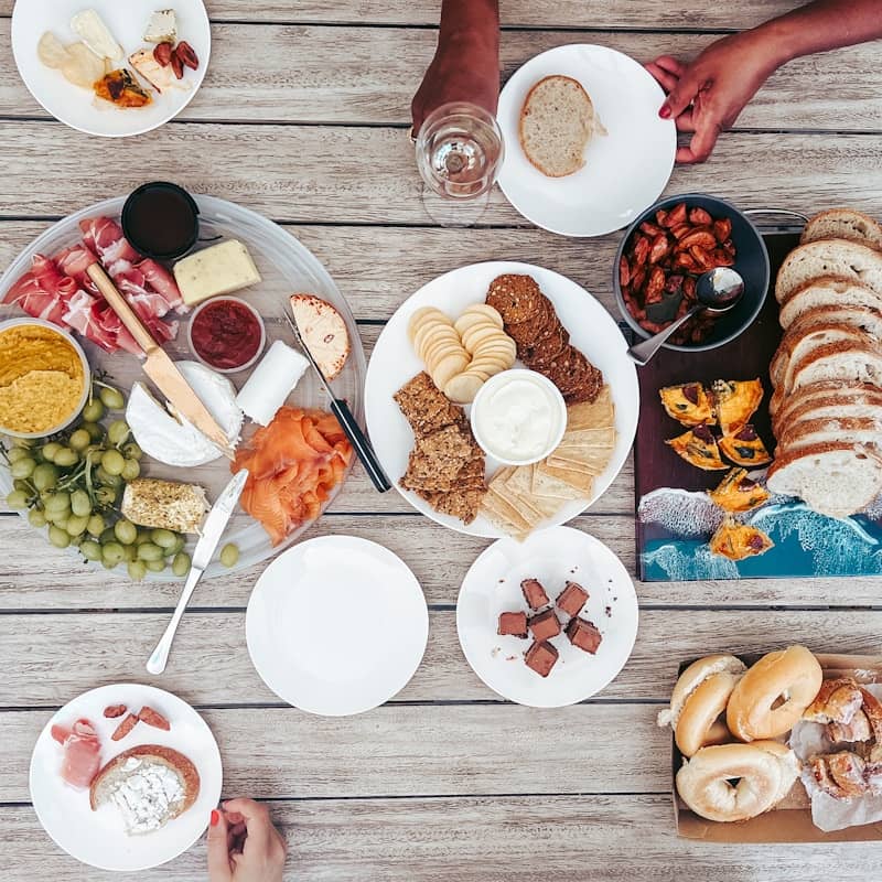 Overhead view of a table with charcuterie, bread, and hands.