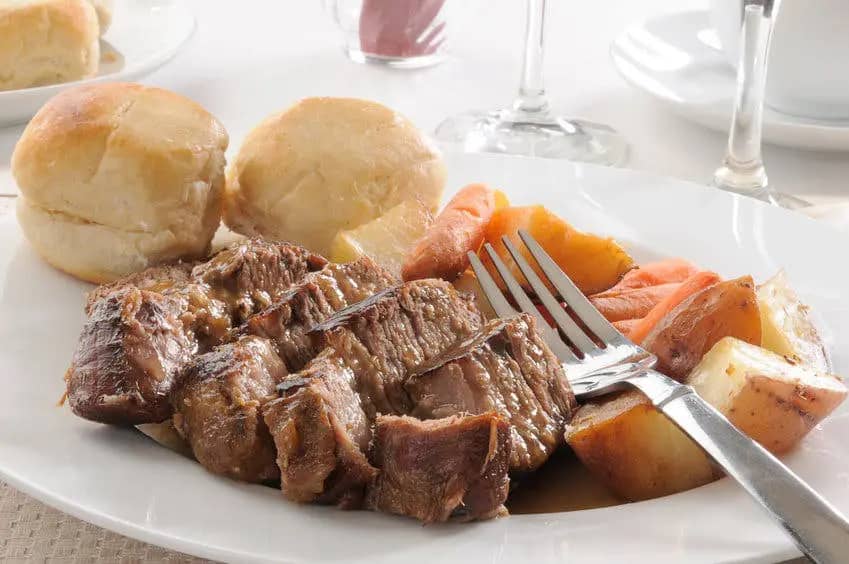 beef pot roast on plate with veggies and rolls