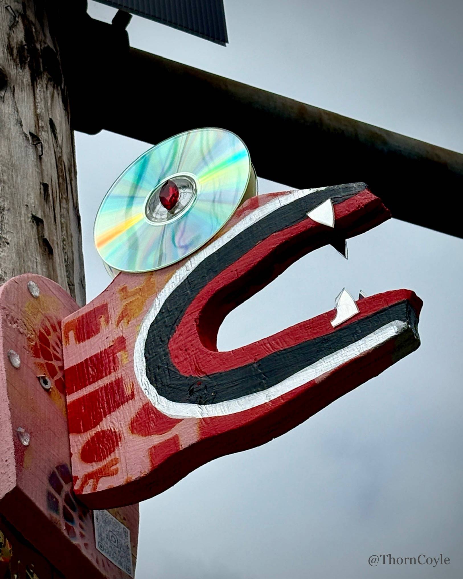 a painted wood dragon head with a CD eye attached to a wood utility pole