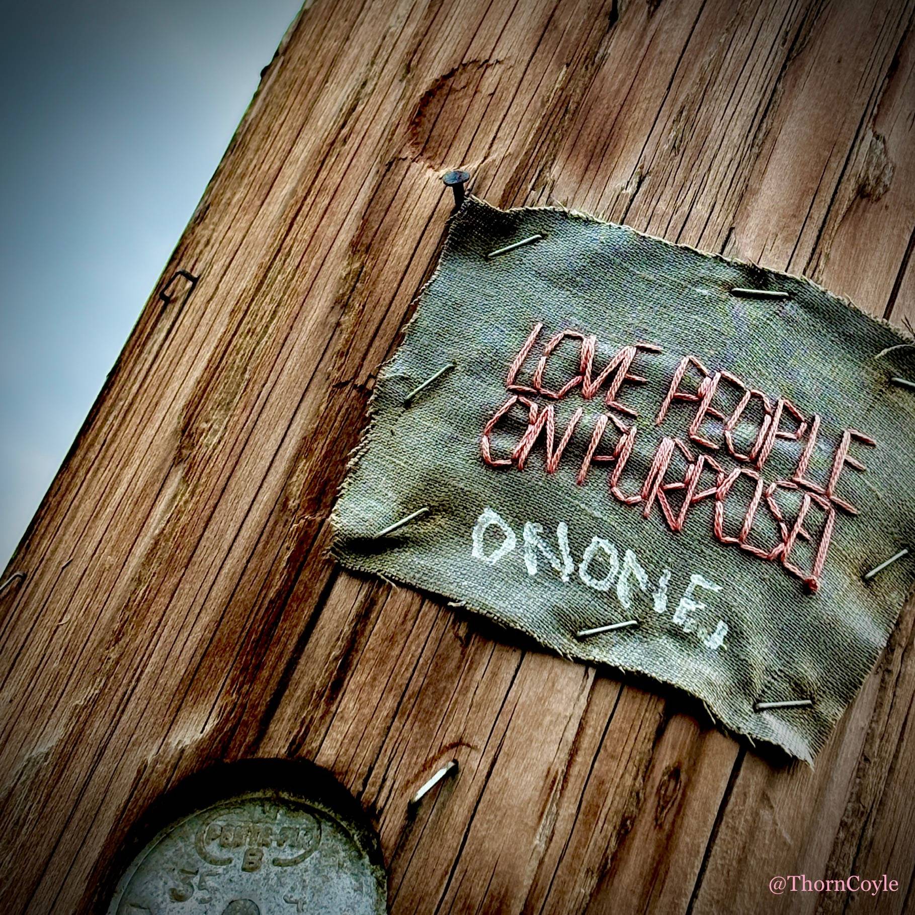 Embroidery stapled to a utility pole: Love People on Purpose