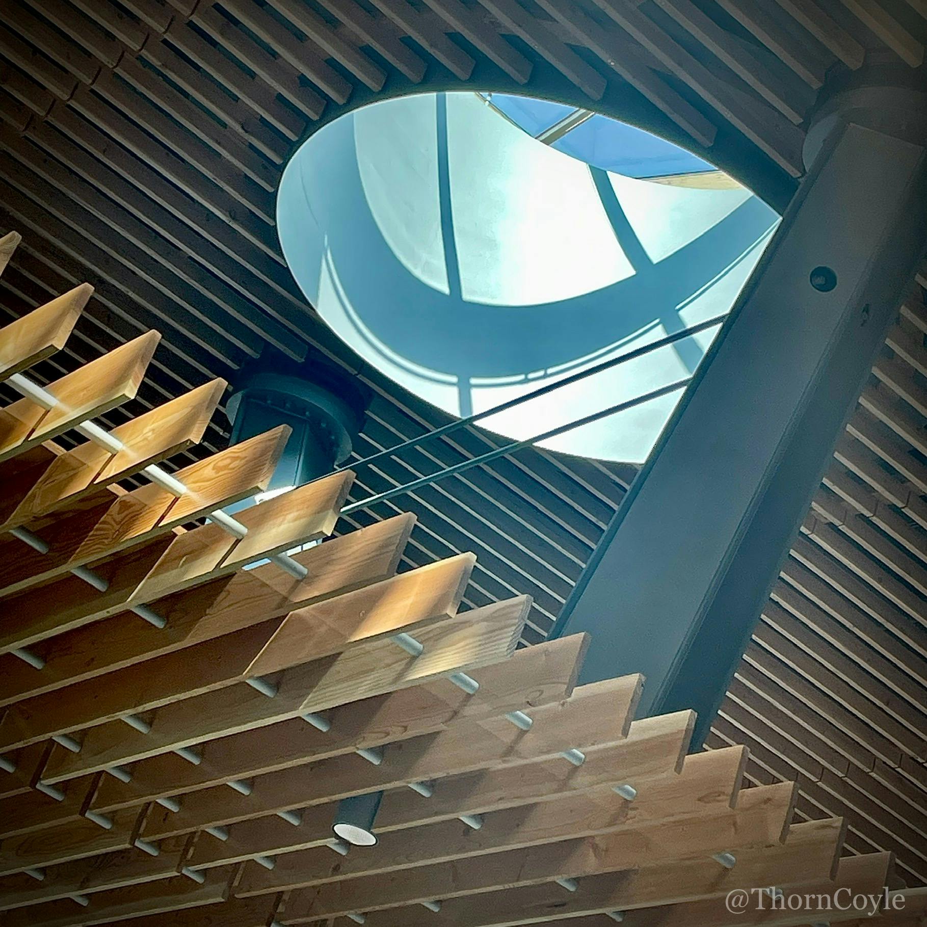 looking up at an industrial ceiling with a large round skylight and wood slats and metal girders