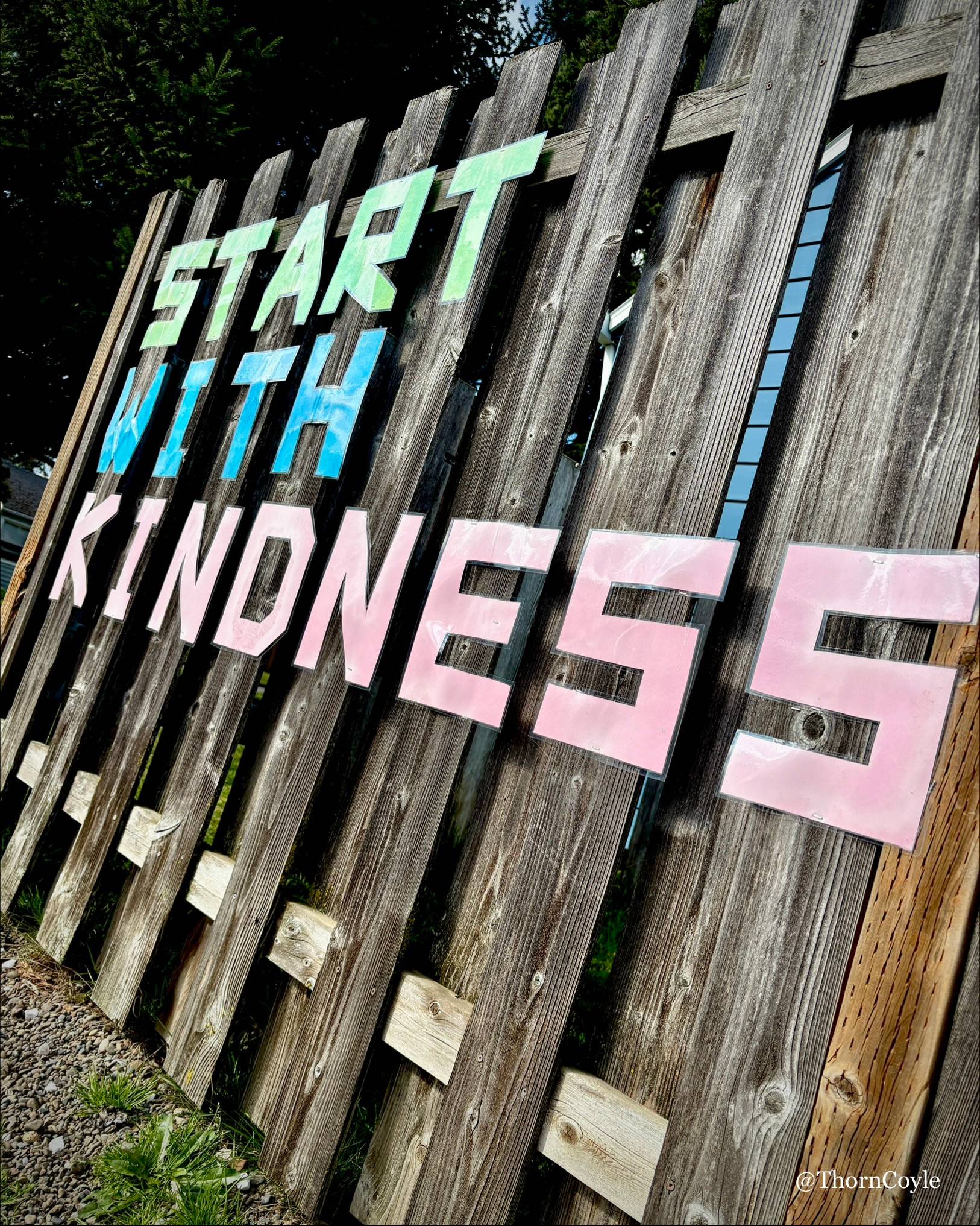 A wood fence with large cut out letters spelling: Start with kindness