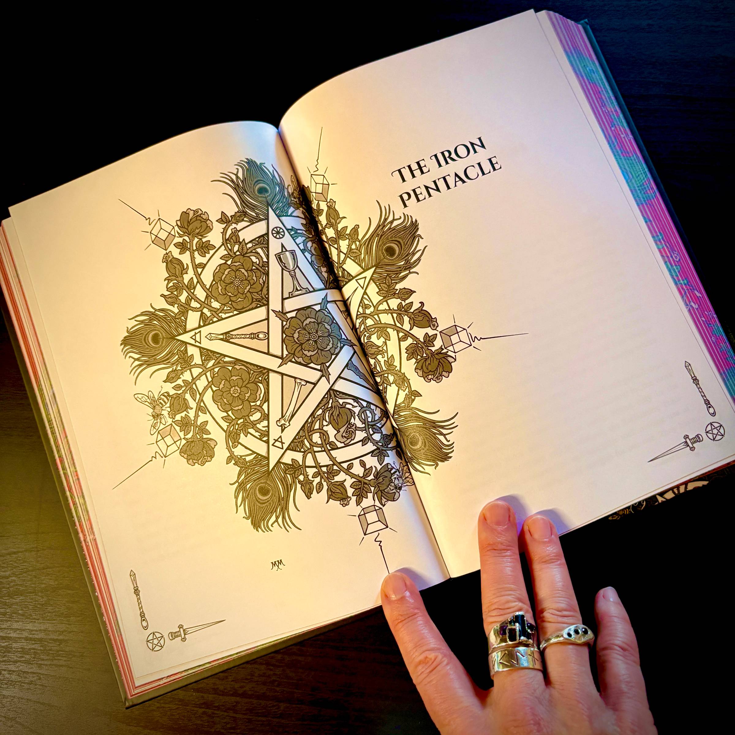 an open book with a double page spread of an ornate pentacle with roses and feathers and colored sprayed edges
