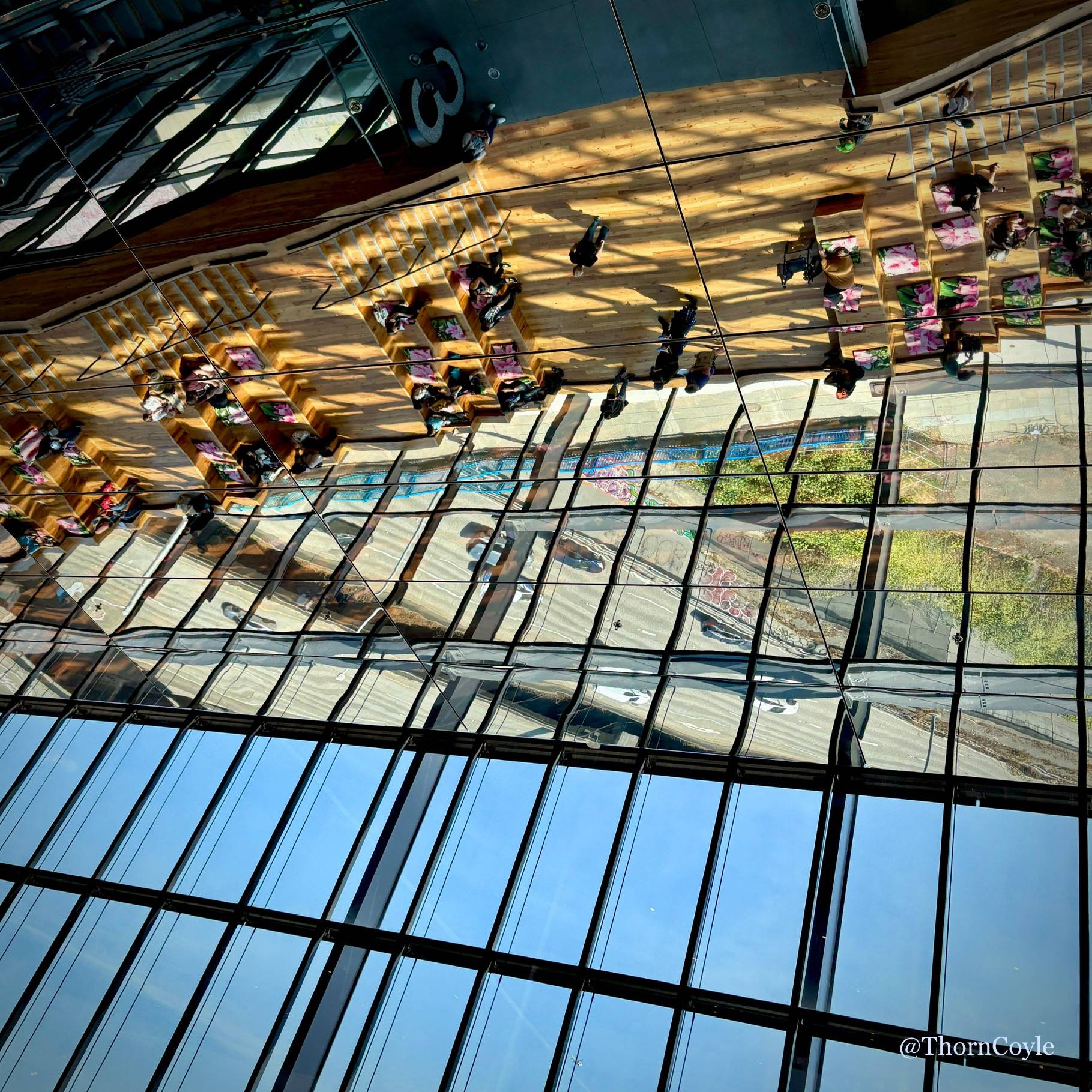 People and cars reflected in glass panels on a convention center ceiling.