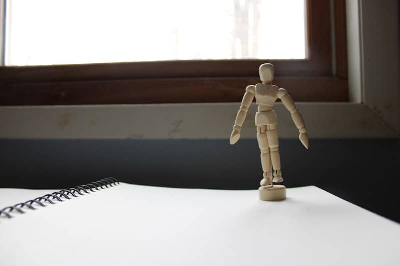 Wooden mannequin figure standing on a notebook.