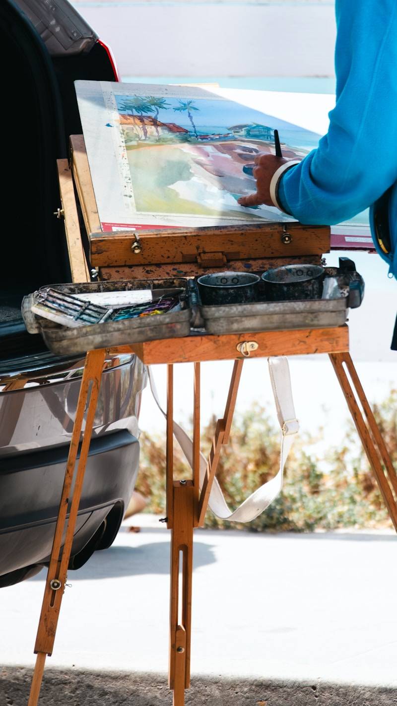 Artist painting a beach landscape on an easel outdoors.