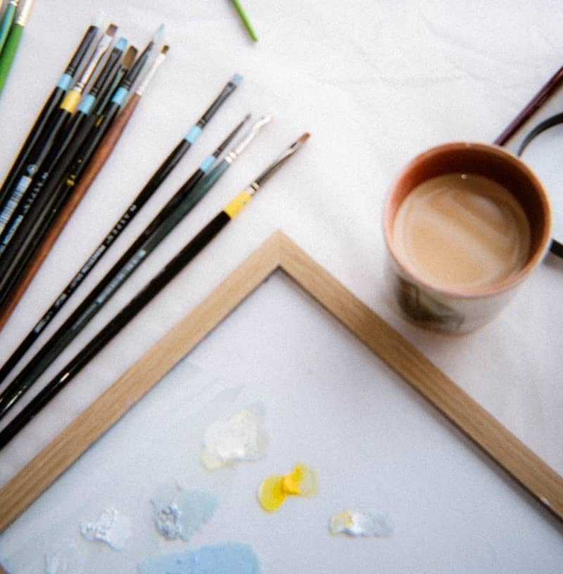 An artist's workspace with brushes, paint, and coffee.