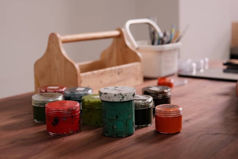 Colorful paint jars and art supplies on a wooden table.