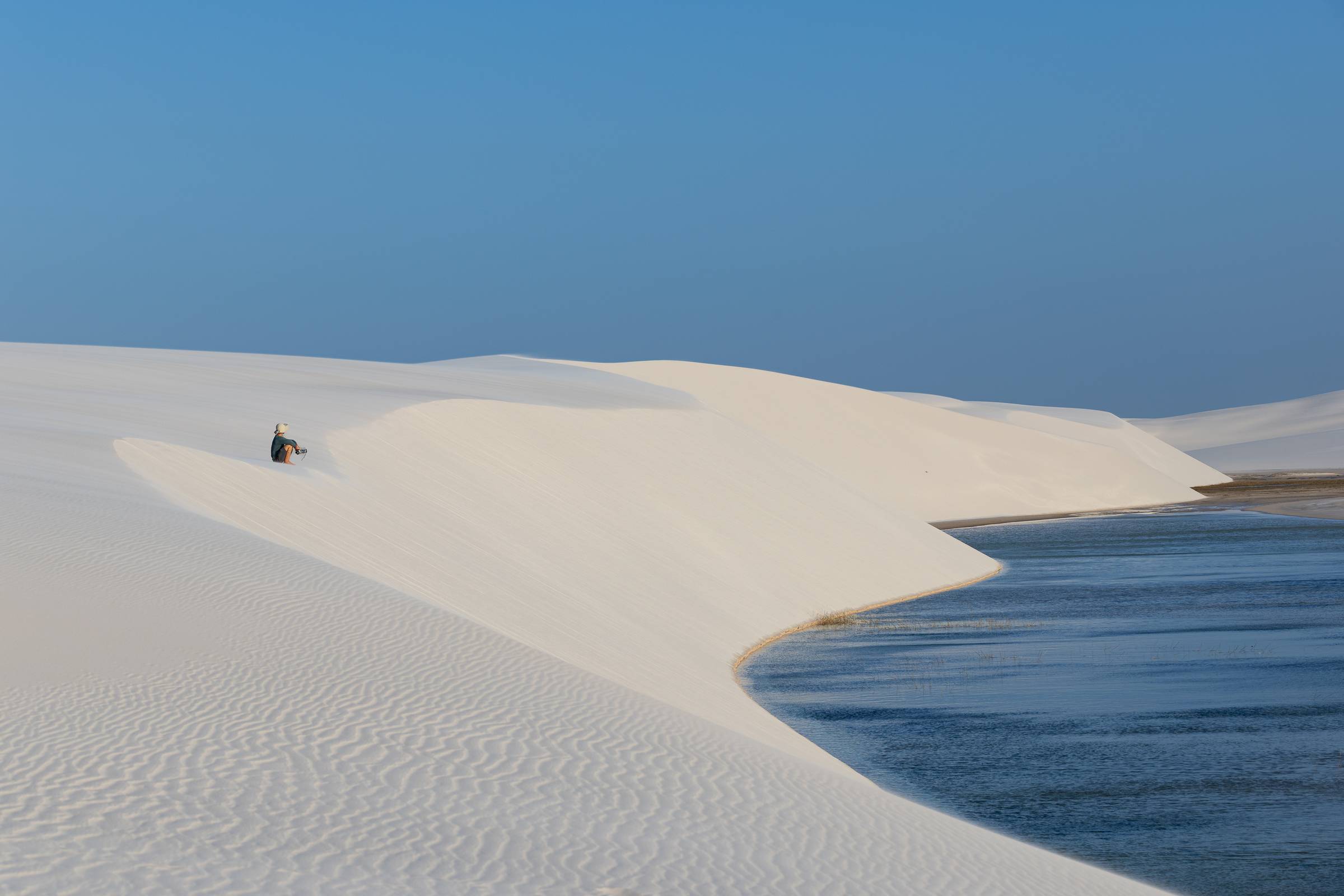 Fotógrafo Ale Rodrigues reflexivo sob a duna durante a expedição fotográfica no Parque Nacional Lençóis Maranhenses