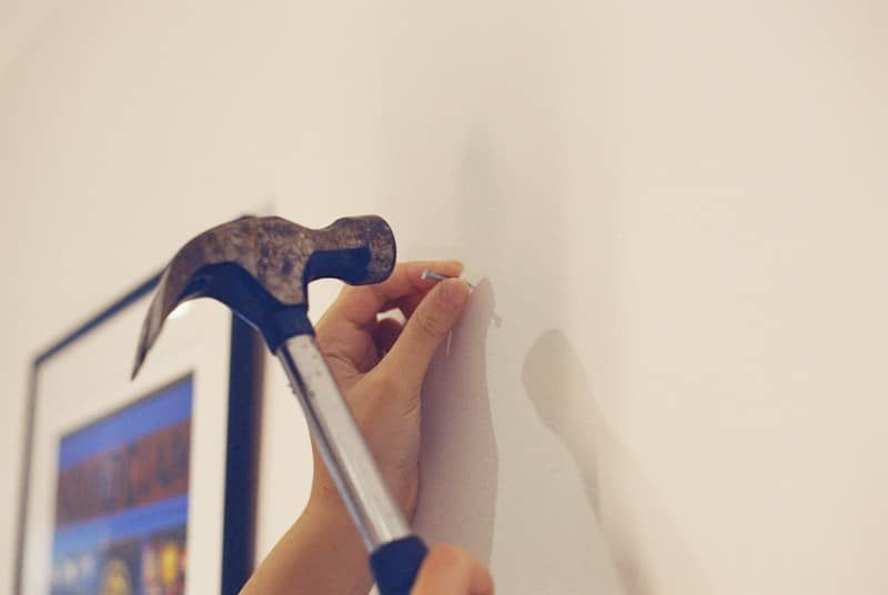 A hand holding a nail against a white wall with a hammer raised