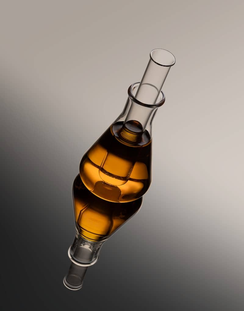 A glass flask with amber liquid reflected on a surface.