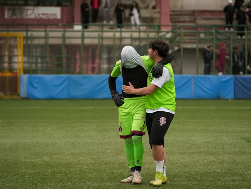 Two soccer players embrace on a field.