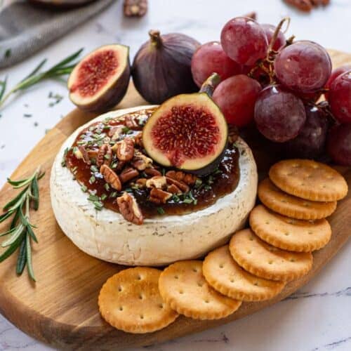 Baked wheel of brie topped with ham and pecans and figs. 