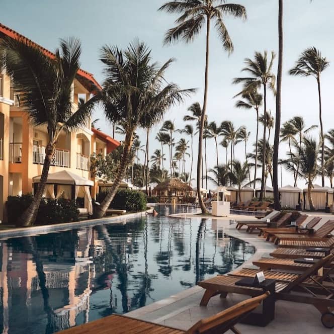 brown wooden lounge chairs near pool surrounded by palm trees