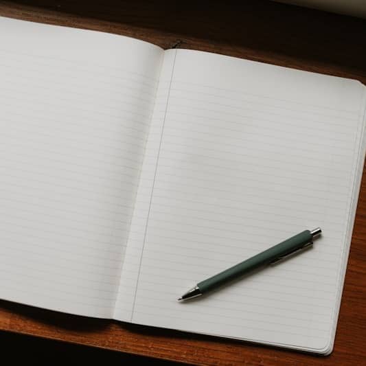Open notebook with pen and pencils on desk