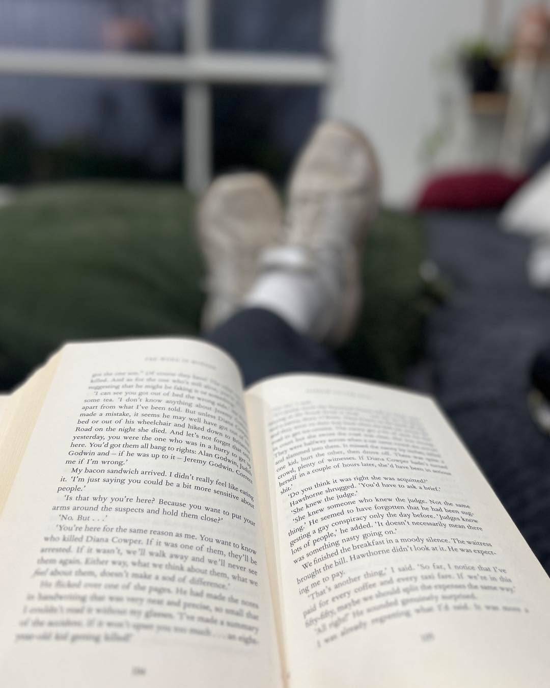 Sitting back in a chair, feet up, reading a book
