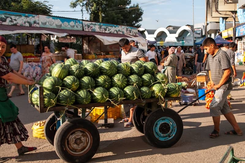 People transport watermelons on a cart at a market.