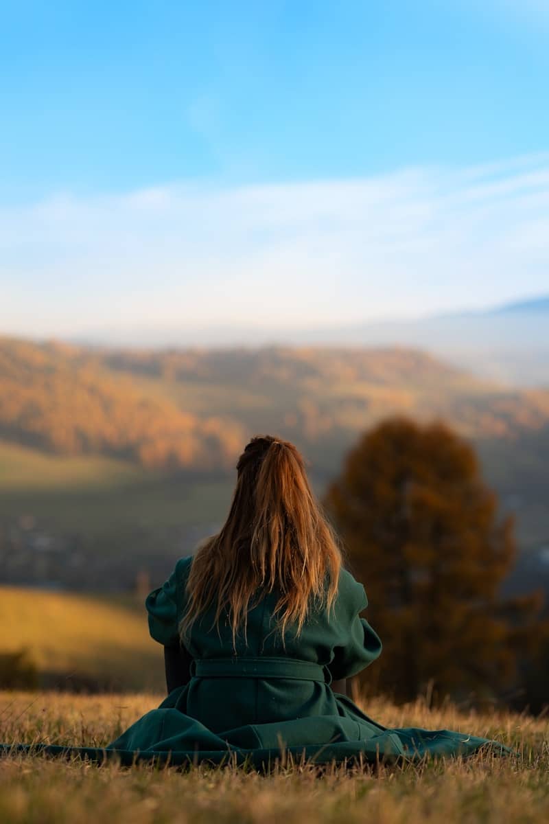 A woman in a green coat sitting on a hill