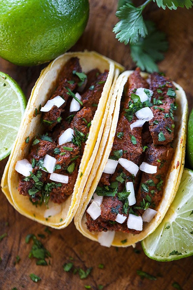 Garlic Guajillo Steak Tacos served in yellow corn tortillas and topped with cilantro and white onions with lime.