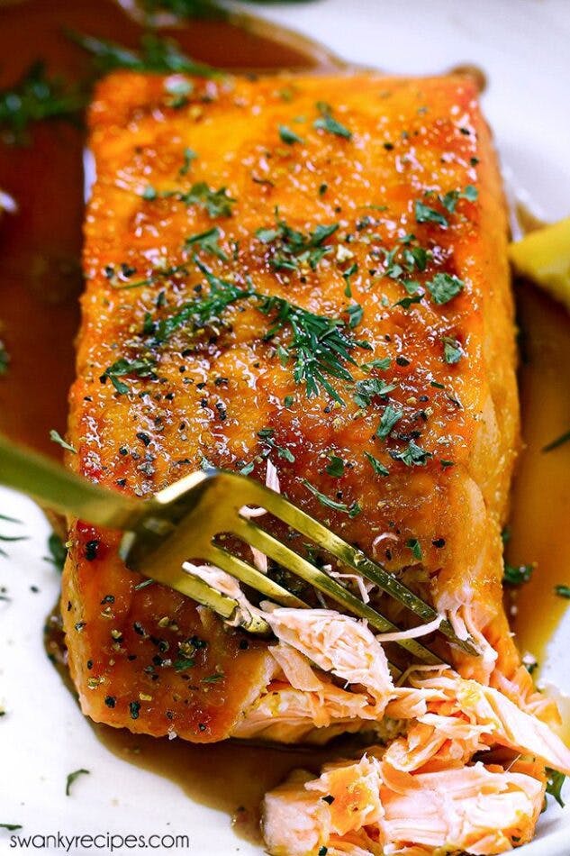 A salmon fillet cooked in the air fryer for 8 minutes and glazed in a asian garlic sesame honey soy sauce. A fork sliced into the center shows the flaky center of the salmon fish.