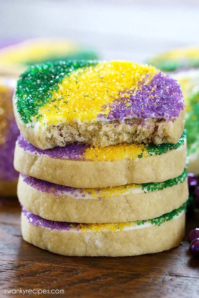 Cinnamon Roll cookies in a stack on a wooden platter. Yellow cinnamon roll cookies with white icing, green, yellow, and purple sprinkles on top.