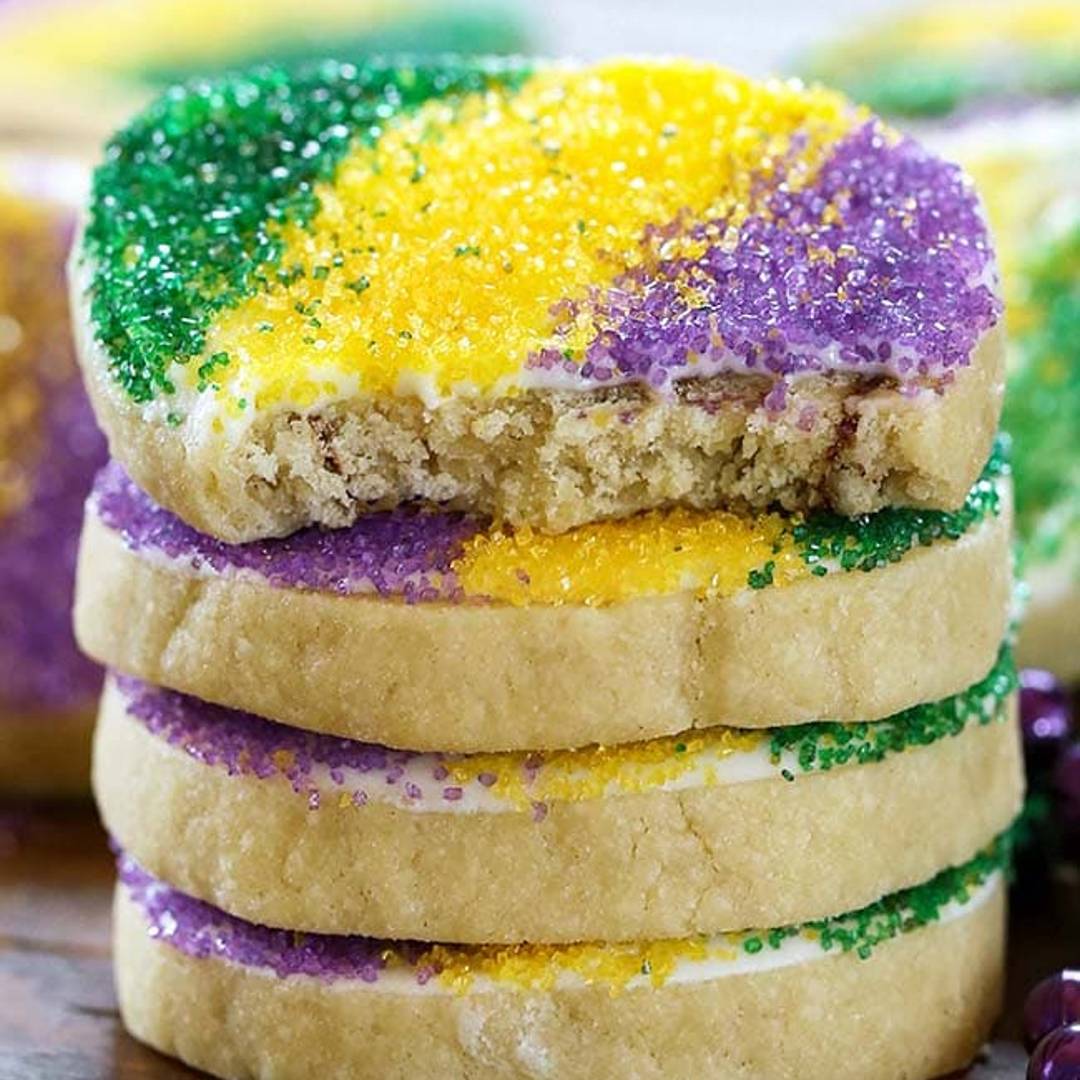 Cinnamon Roll cookies in a stack on a wooden platter. Yellow cinnamon roll cookies with white icing, green, yellow, and purple sprinkles on top.