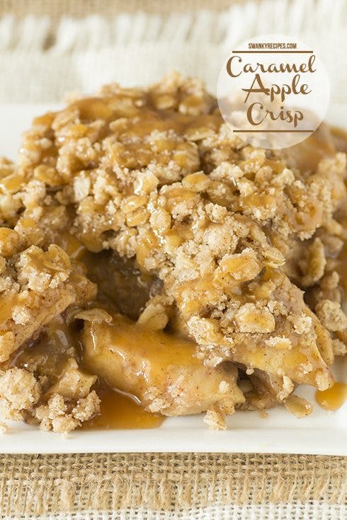 Golden-brown Caramel Apple Crisp in a baking dish, glistening with caramel drizzle, surrounded by fresh red apples and autumn leaves.