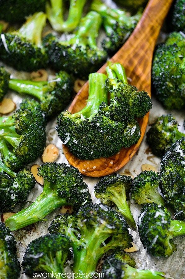 Close-up view of Crack Broccoli topped with grated Parmesan cheese, held on a wooden spoon against a blurred background