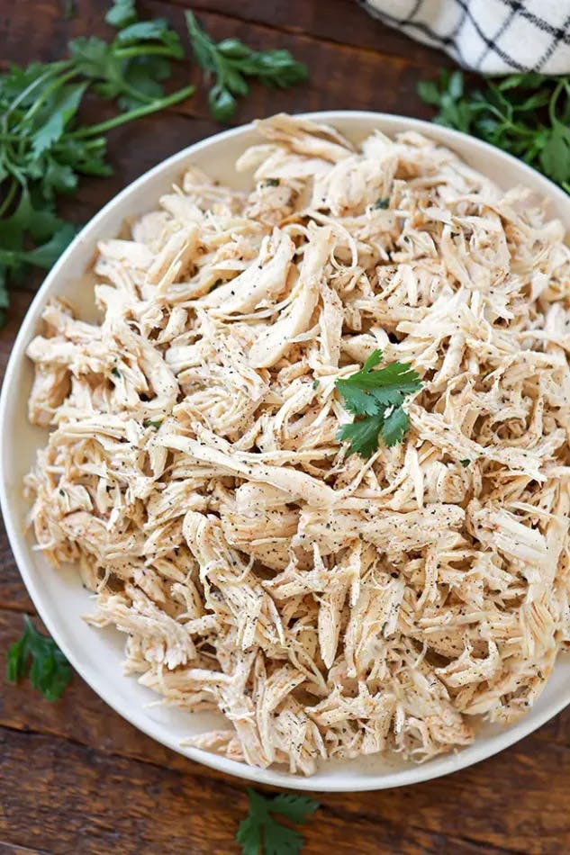 A bowl filled with tender shredded chicken, beautifully garnished with fresh parsley leaves, highlighting the texture and moistness of the chicken.
