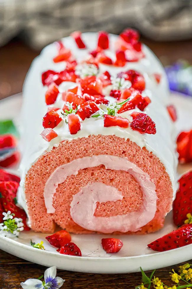 A beautifully sliced Strawberry Roll Cake showcasing layers of moist sponge cake and luscious strawberry filling, topped with a dusting of powdered sugar