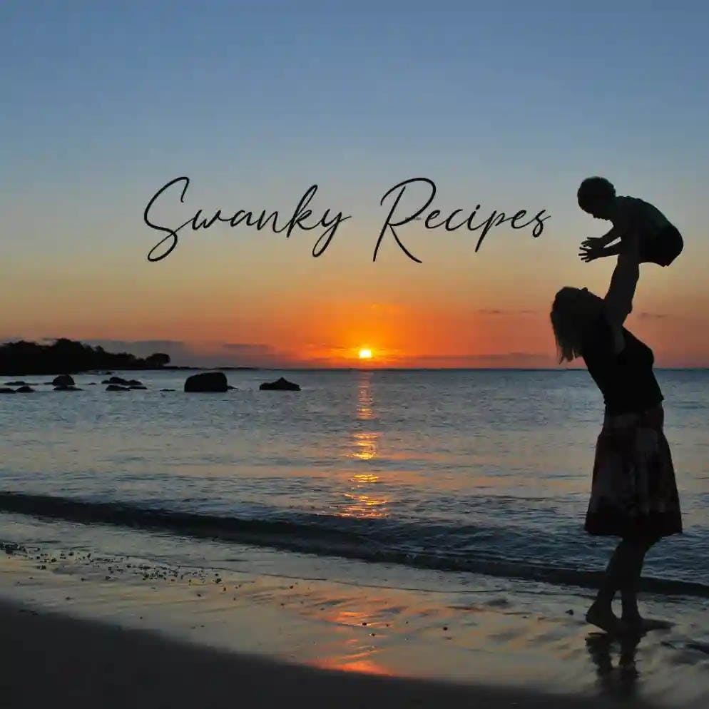 A heartwarming image of a mother holding her baby on a serene beach, with the golden sun setting in the background. The Swanky Recipes logo is centered in the image, adding a touch of elegance to the overall aesthetic