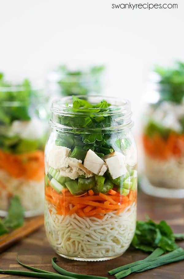 Instant ramen noodles in a mason jar with shredded carrots, celery, deli sliced chicken, celery leaves, green onions, and snow peas. 