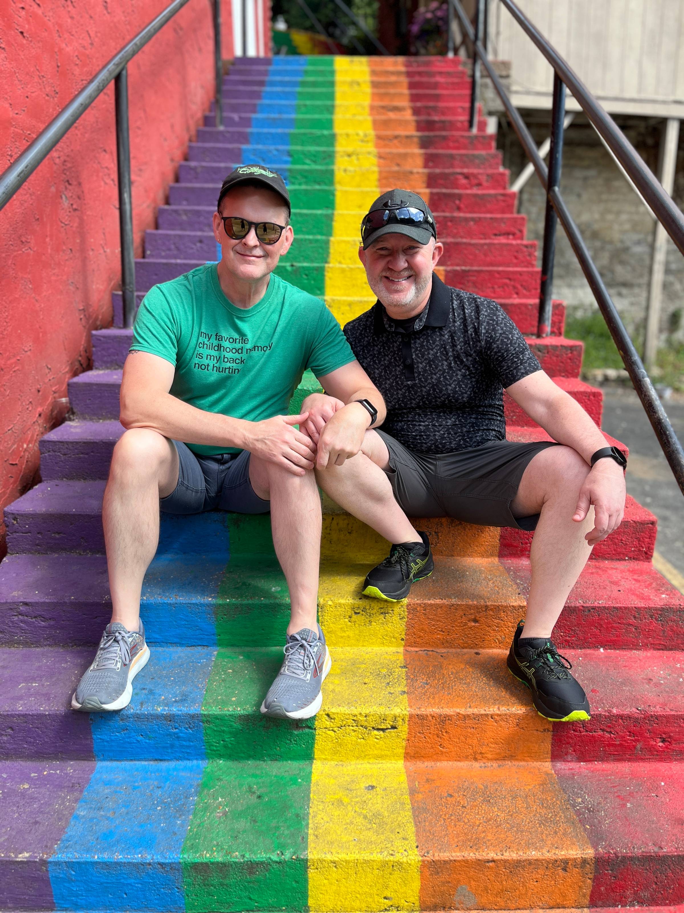 Me (on the left, in sunglasses) and my partner Michael sitting on a staircase painted in rainbow colors. Because gay. Like, really gay. So gay. Gay gay gay.
