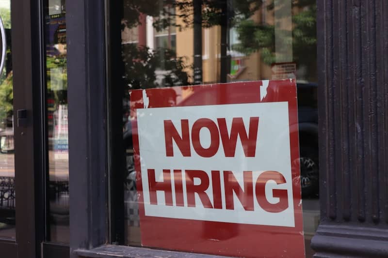 A "now hiring" sign hangs in a store window.