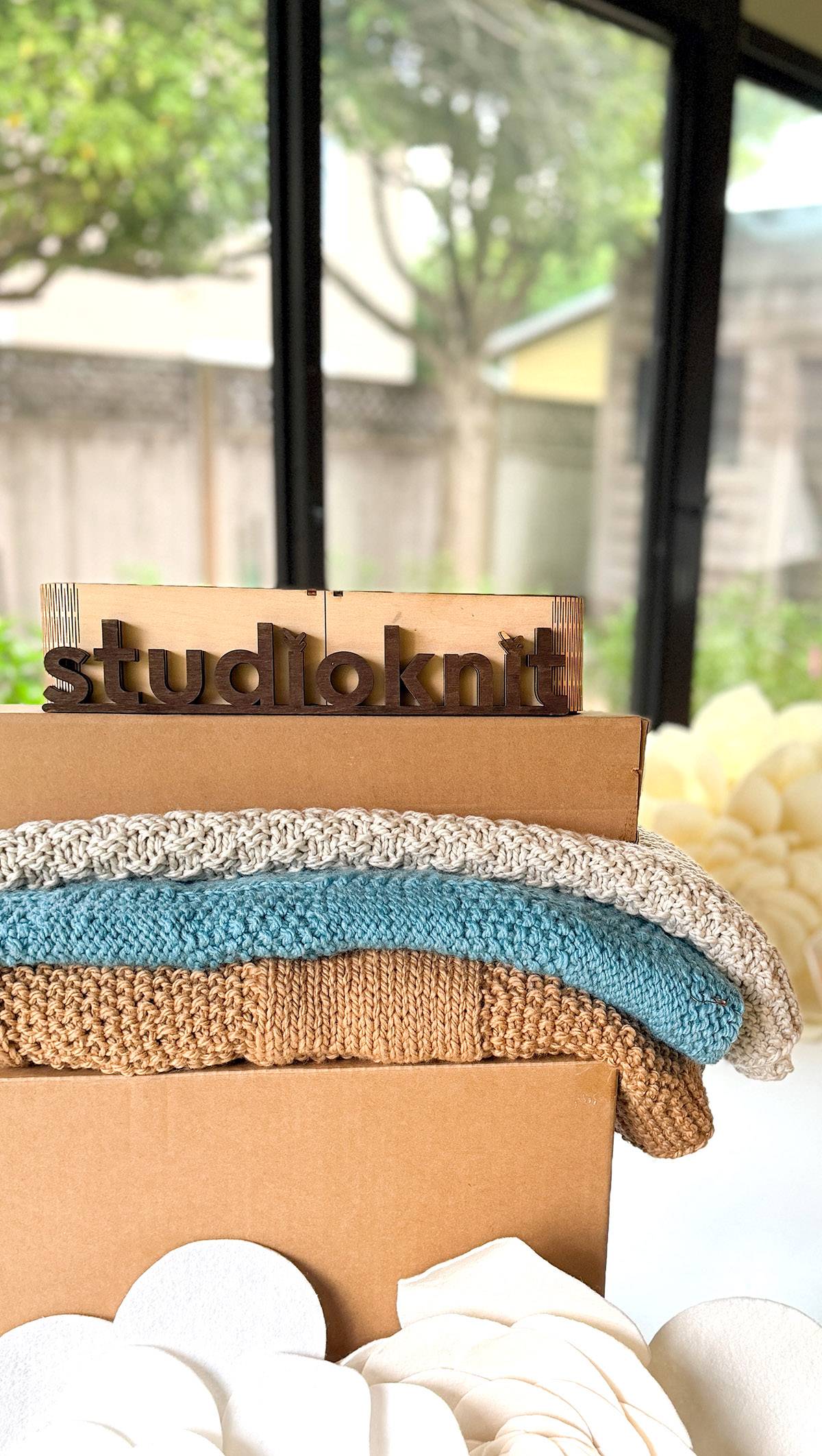 Folded hand-knit blankets stacked on shipping boxes in the Studio Knit workspace.