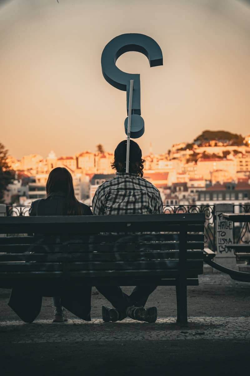 Two people on a bench with a large question mark